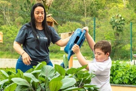 Criança regando planta com a ajuda da professora